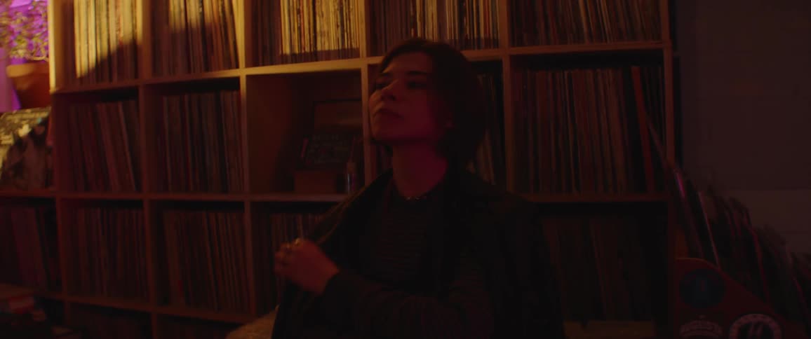 A woman chews on her nails as she sits in a room with bookcases