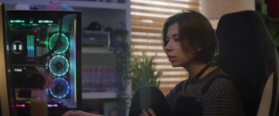 A teenage girl sits at home and nods her head as she looks at her computer