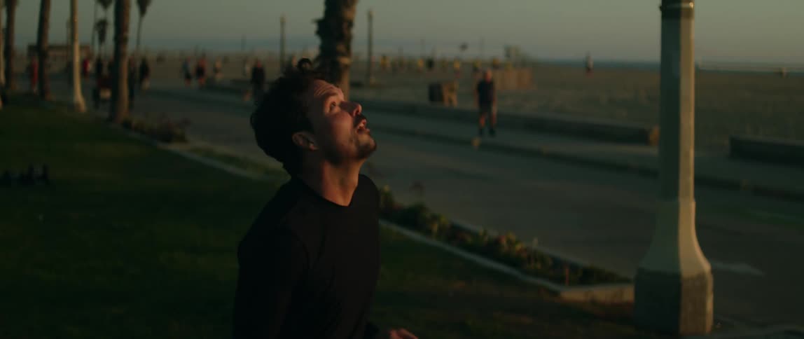Man plays around with a soccer ball in park across road from busy beach