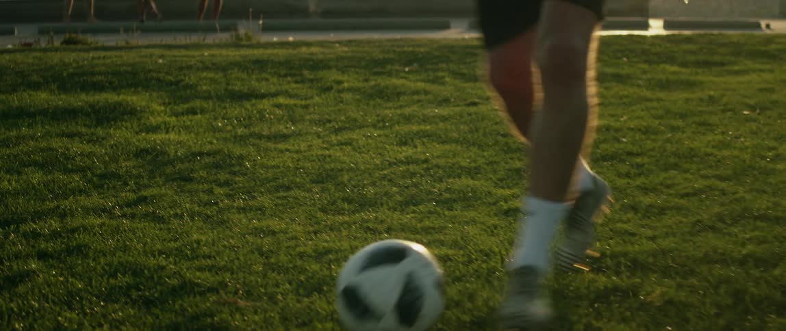 Man practices with soccer ball as two people on scooters pass on road behind him