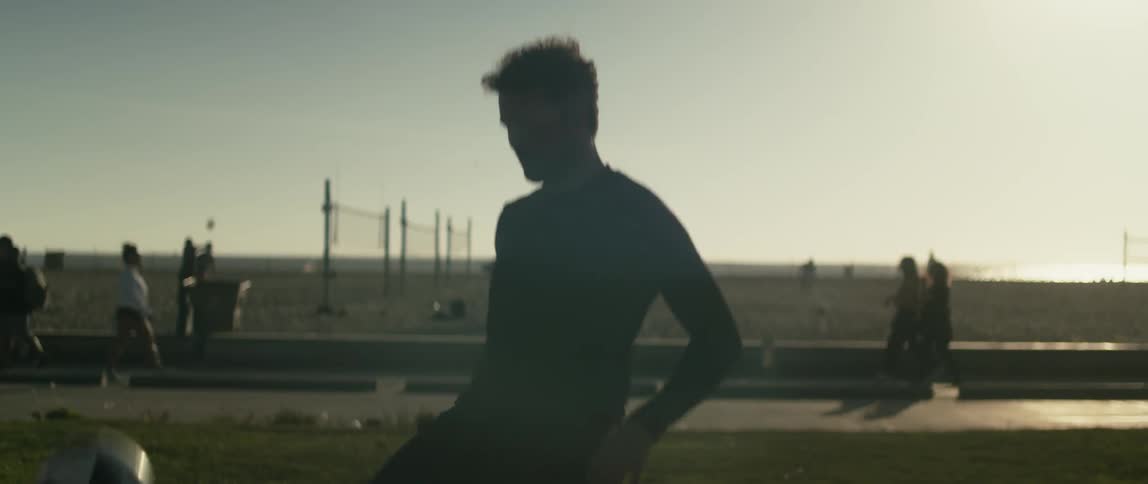 A man kicking around a soccer ball on a grassy lawn near a beach