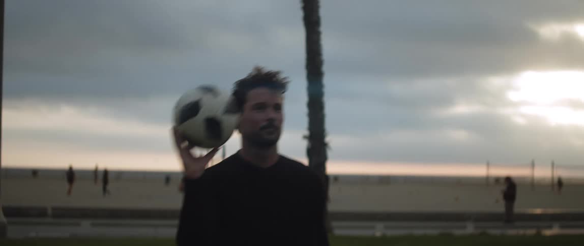 A man playing with a soccer ball outside at sunset