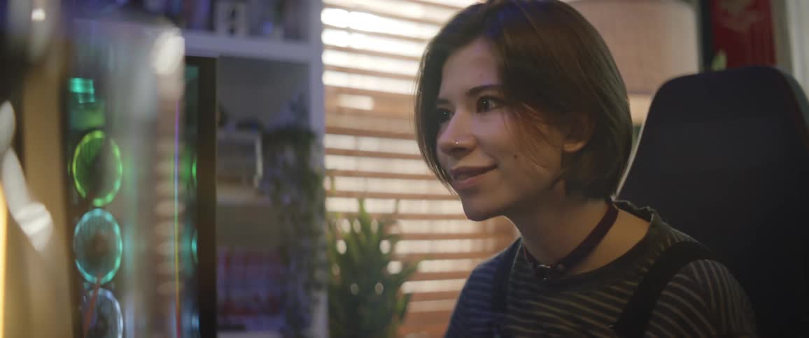 A woman is smiling as she sits in front of a gaming computer