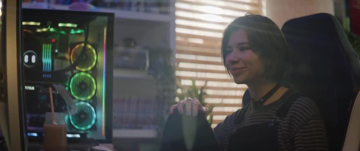 A teenage girl sits in front of a computer at home and talks and waves at the screen