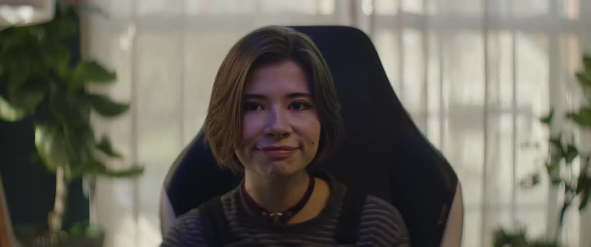 A teenage girl is sitting in a chair and she waves