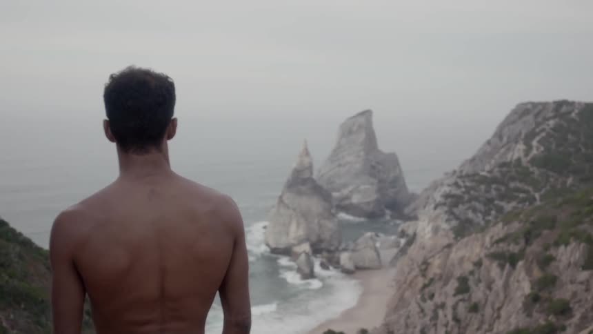 Man standing high above a beach looking down on it