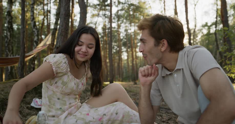 A couple eat grapes while picnicking in the woods
