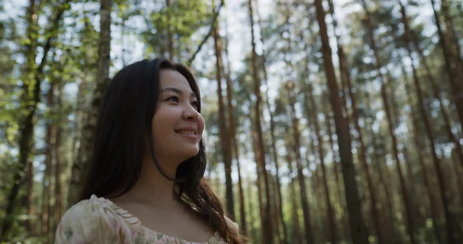 Man and woman stand in woods holding hands and smiling at each other