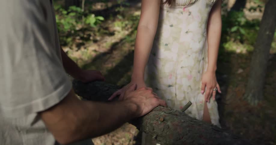 Man wearing white shirt and woman with white floral dress thick tree branch in the woods