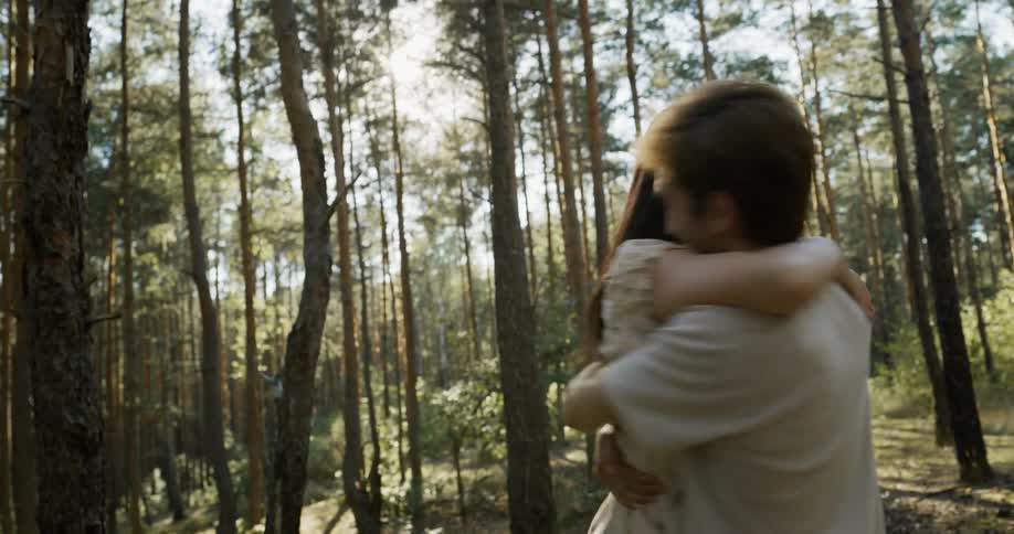 A teenage couple are in the woods as the male lifts the female hugs her and spins her around playfully a few times