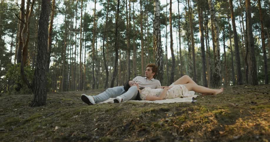 Man and woman lie together on ground on blanket in woods