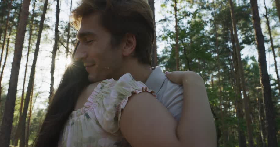 A man and a woman are hugging each other as the sun shines through the trees in the woods