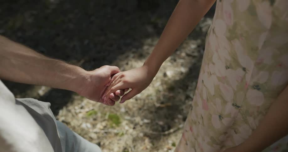 A man and a woman are standing together in the woods and he reaches out and holds her hand