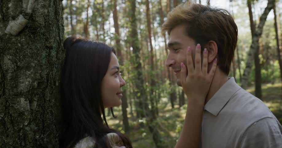 Woman puts her hand on face of man as they face each other in the woods