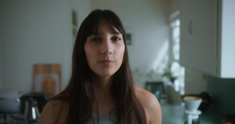 A young woman stands in her kitchen at home and smiles