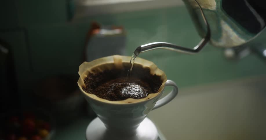 Hot water pouring over coffee being brewed on a filter directly inside a porcelain cup
