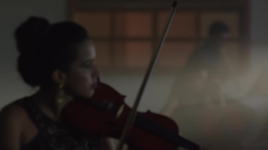 A woman is playing a violin as another woman plays a big bass guitar and a man plays a clarinet
