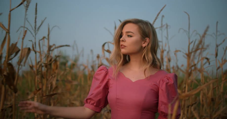 A woman walks through tall corn stalks