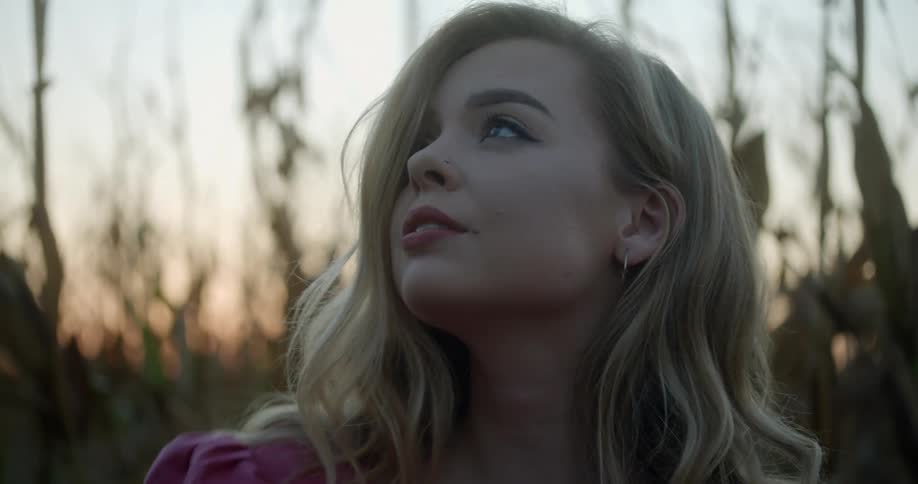 Blonde woman wearing pink blouse looks up in the forest smiling at sunset