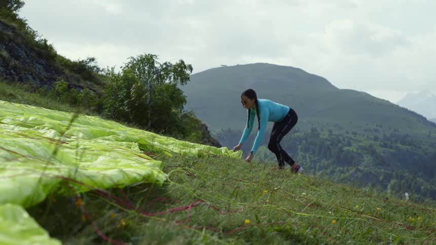 A woman preps a paragliding canopy on the side of a hill
