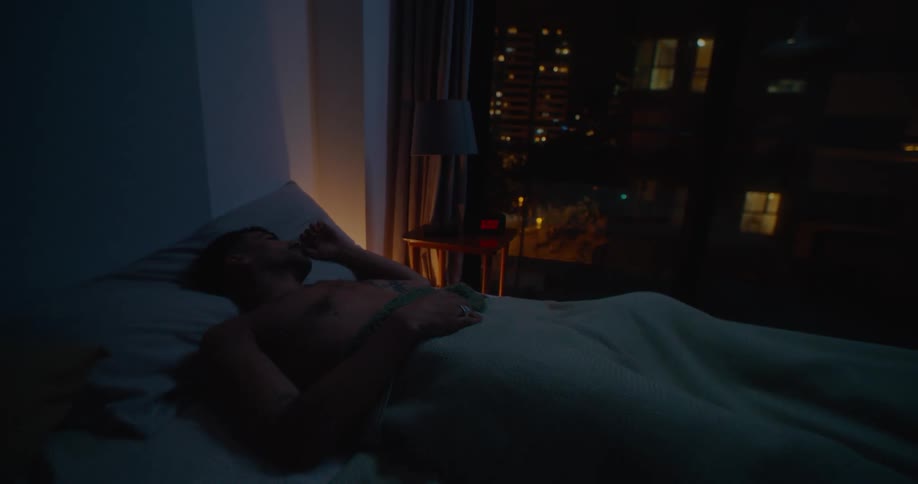 Topless man lies in bed in bedroom at apartment at night