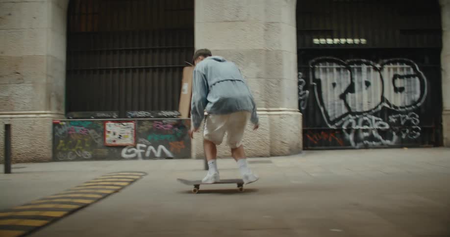 Male skateboarder jumps skateboard over speed bump in alley passing graffiti strewn buildings