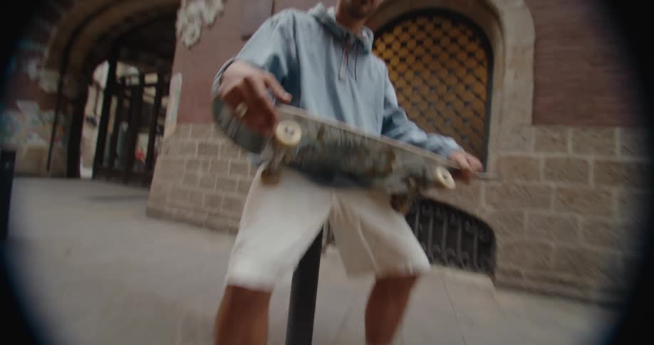 Young man sitting on a pole in a narrow alleyway in the city holding a skateboard