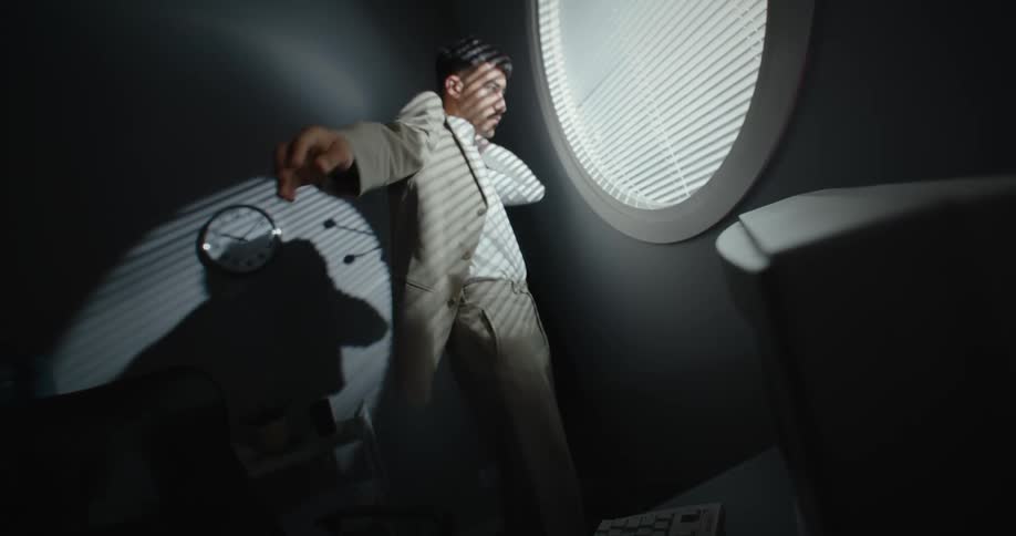 A man looks out a window while putting on a suit jacket