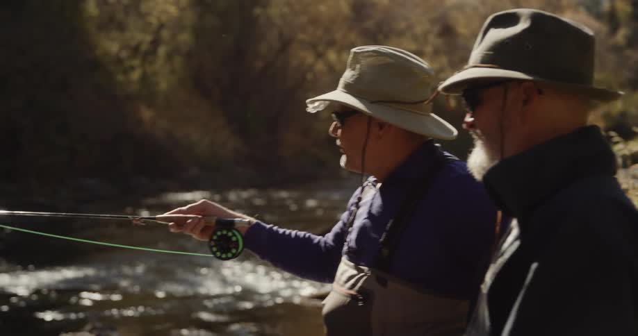 Two elderly men fish in a river