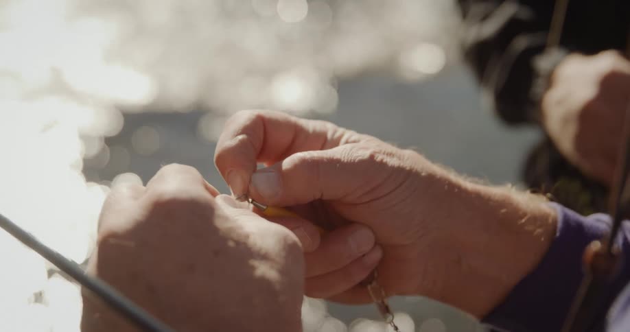 A fisherman attaches bait to fishing wire while standing in water