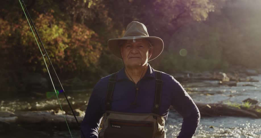 Sunlight shines brightly as a man stands near a river in the woods holding his fishing rod
