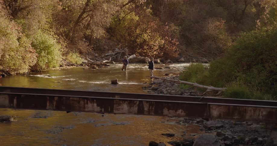 Two elderly men stand in a river and fish