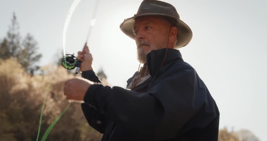 Man stand near trees on a bright sunny day and casts his fishing line