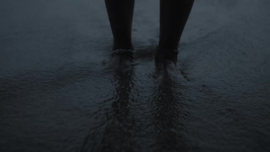 Person standing on a beach allowing the waves to wash over their feet