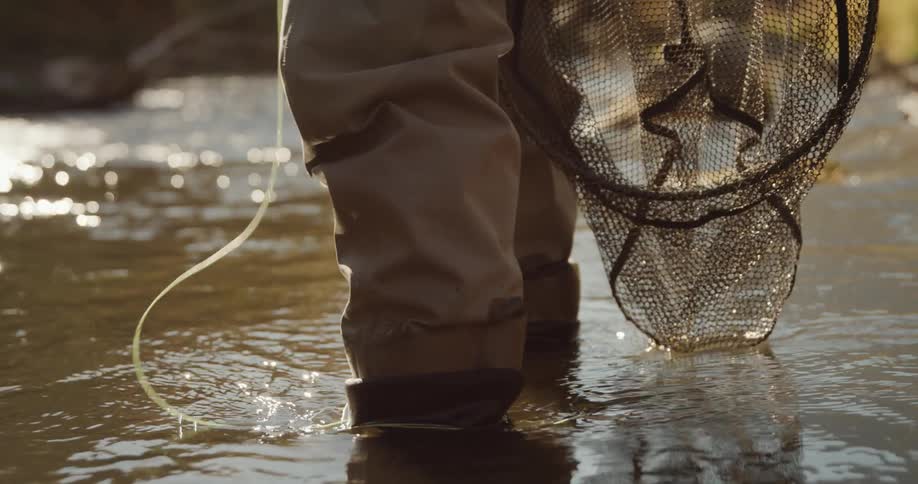 Man with gray pants fishing line and fishing net stands in the forest stream
