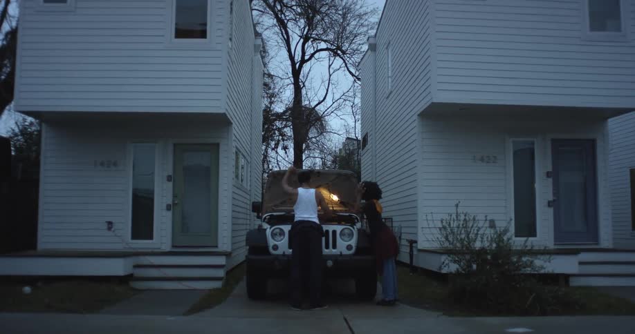 Man and woman opens white jeep car hood between two white buildings in the street