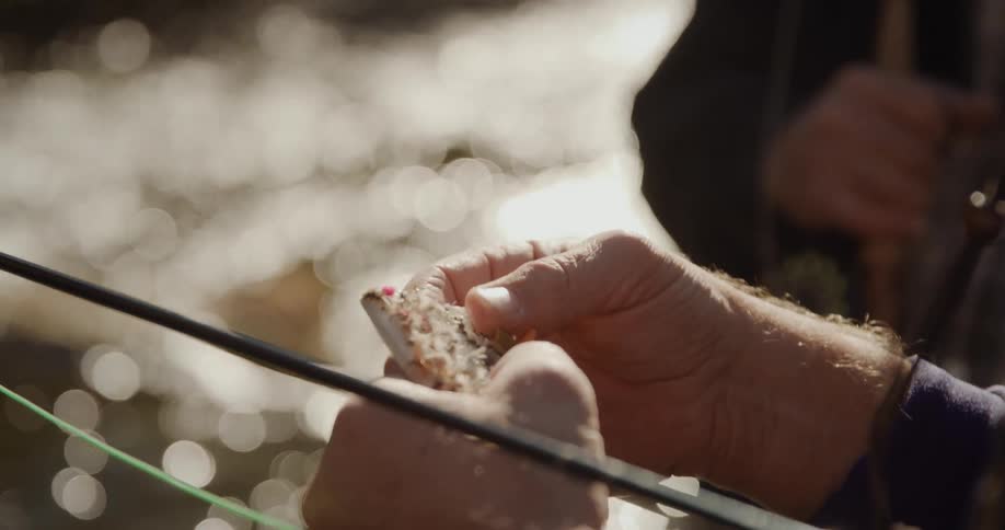 Close up of elderly mans hands hooking a piece of bait on the fishing poles hook in the stream