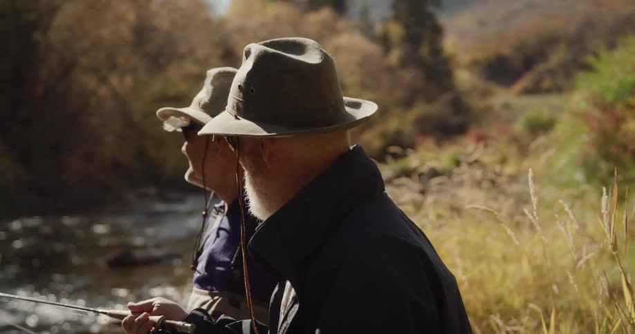 Two men wearing hats and sunglasses fishing on a river at morning