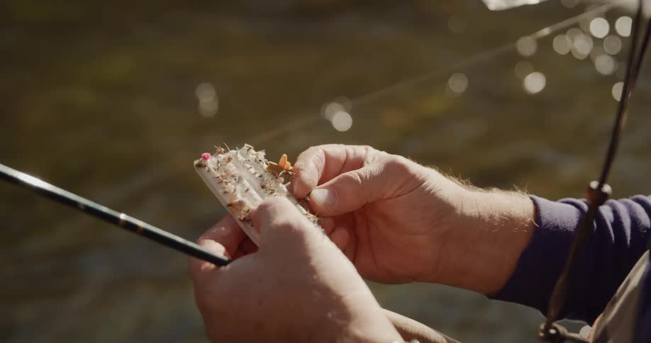 Man attaches a lure to a line on a fishing rod near a river