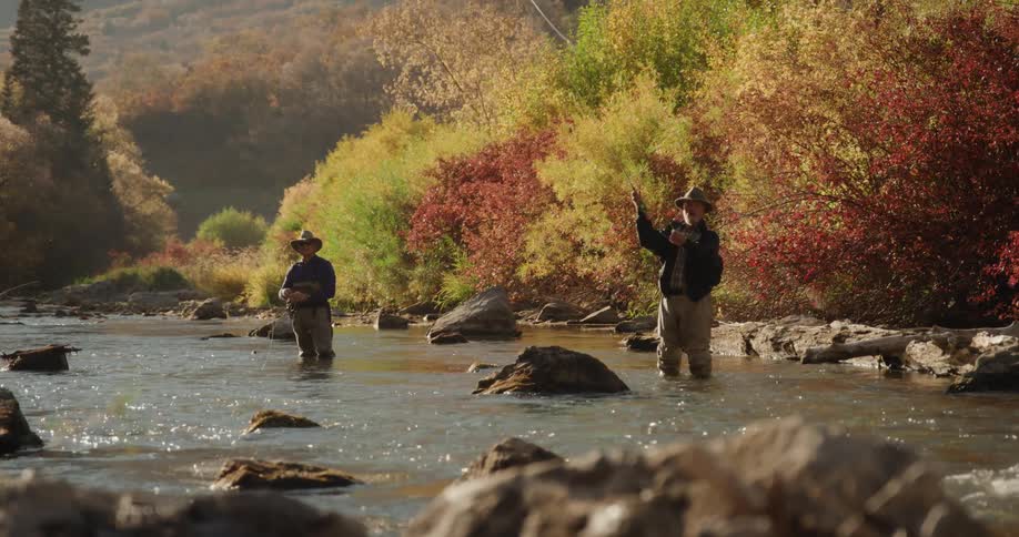 Two men are casting their fishing lines in the river surrounded by trees in fall colors
