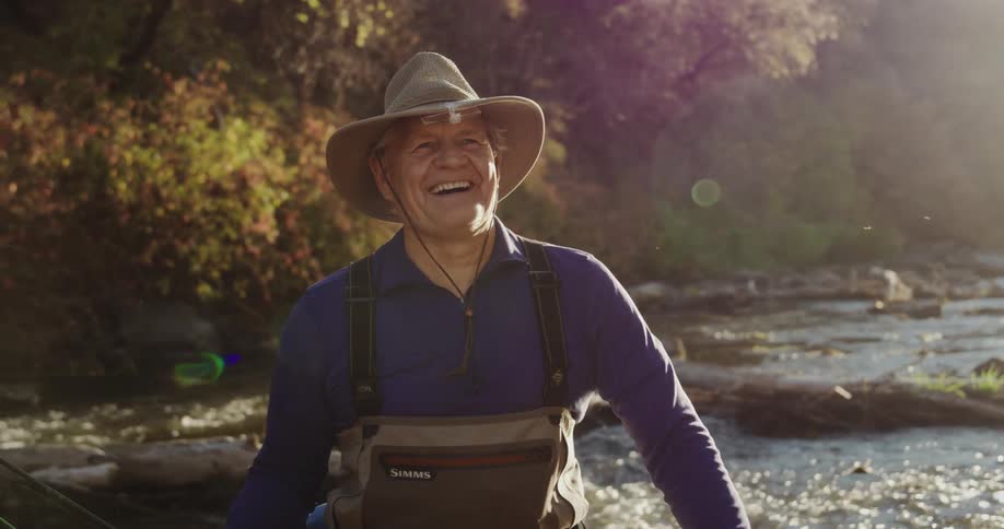 A fisherman laughs while standing in a river