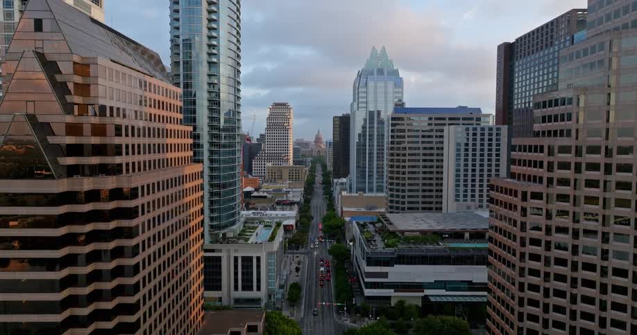Traffic moves down treelined downtown streets near park under a cloudy sky