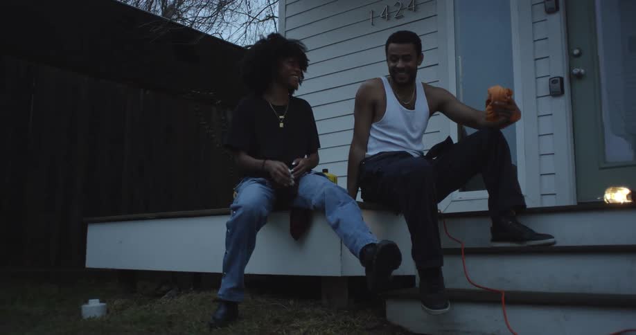 A man and woman chat while sitting together on the porch of a house in the evening