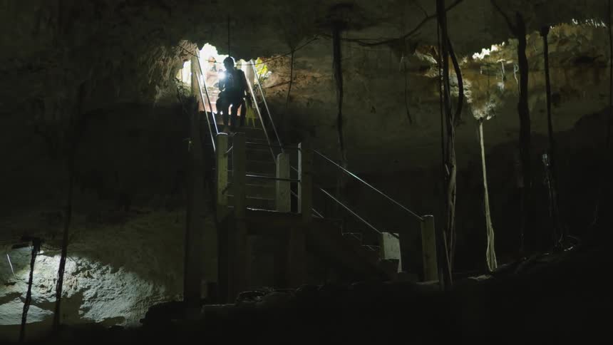 A person is walking down a flight of stairs inside a cave