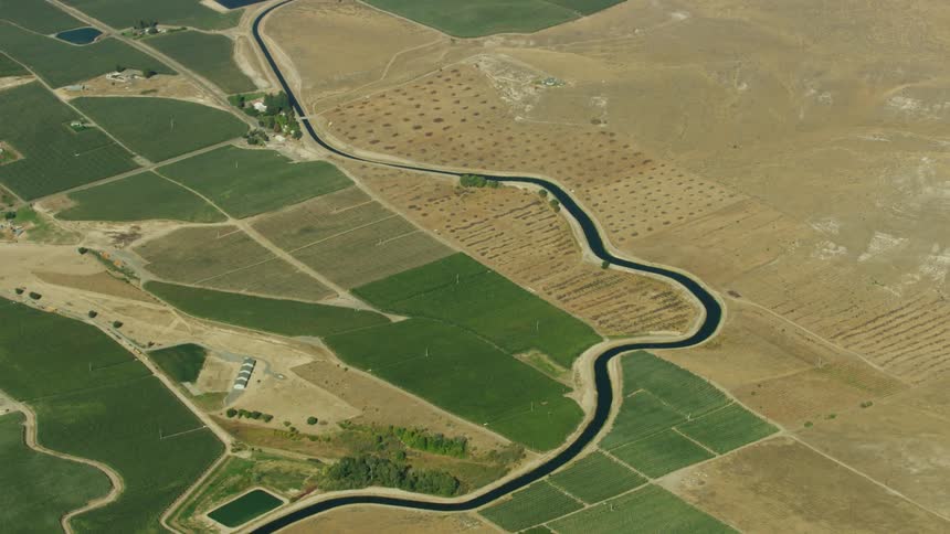 An irrigation canal weaves through the arid desert and geometric farmland parcels