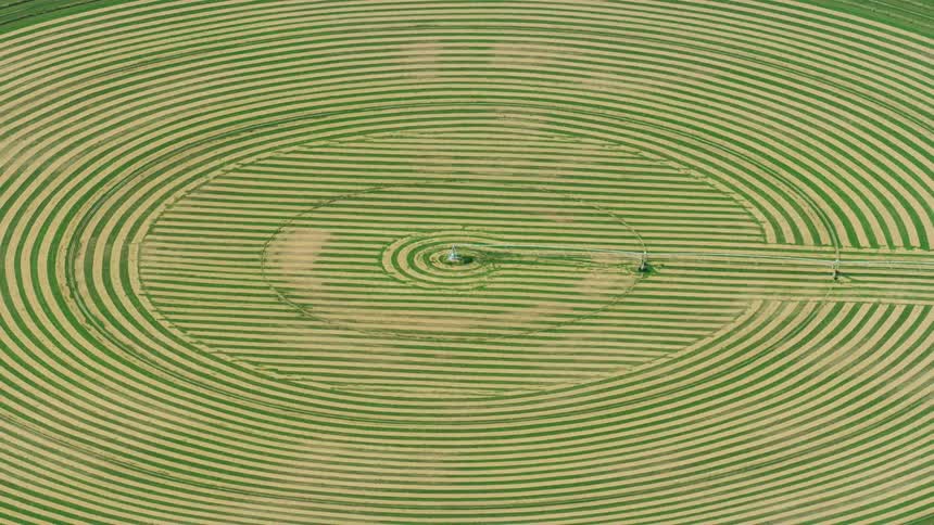 Slow zoom out aerial of center pivot irrigation circles revealing a wide perfectly symmetrical pattern of harvested alfalfa