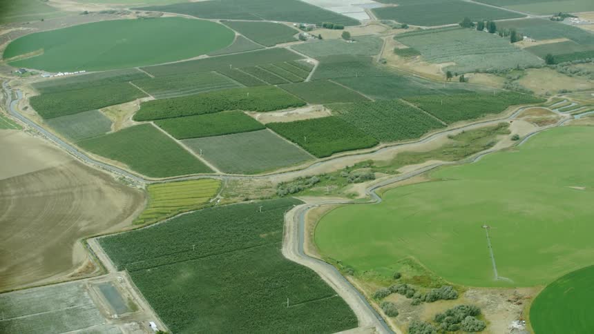 An irrigation canal and small stream weave through varying fields and orchards of irrigated agriculture and crop land in the arid desert of the western USA