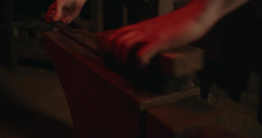 A man uses a large brush to scrub wood in a dark room
