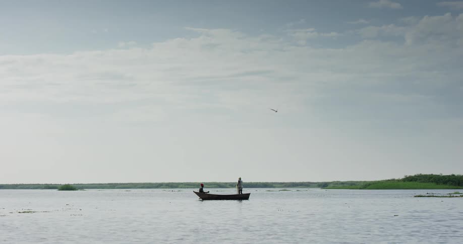 Two people stand and sit on a boat stopped in the middle of a lake