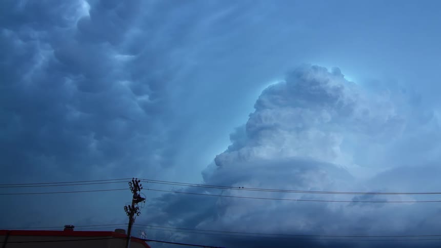 Cables stretch across utility poles near a building as clouds move in the sky above
